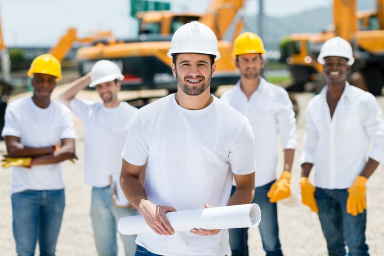 Architect with a group at a construction site holding blueprints